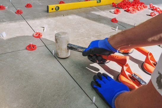 Un carreleur professionnel en polo bleu pose des carreaux de céramique blancs sur un mur de salle de bain